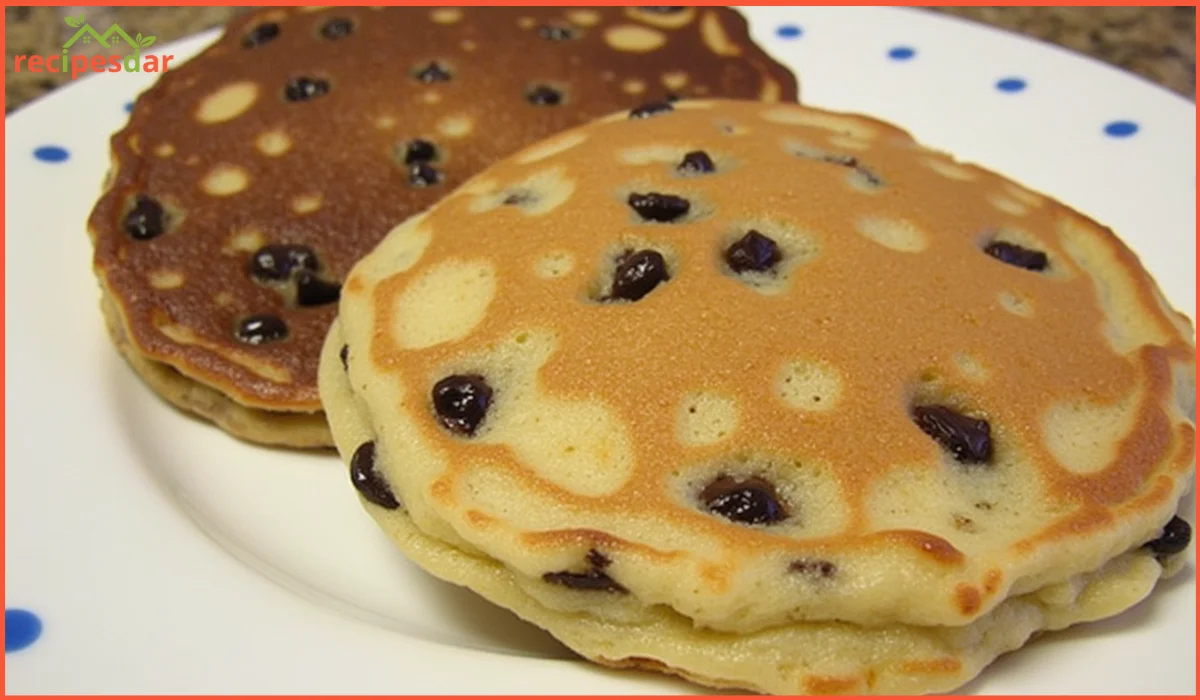 Golden sheet-pan chocolate chip pancakes sliced into squares, topped with fresh berries and a drizzle of maple syrup