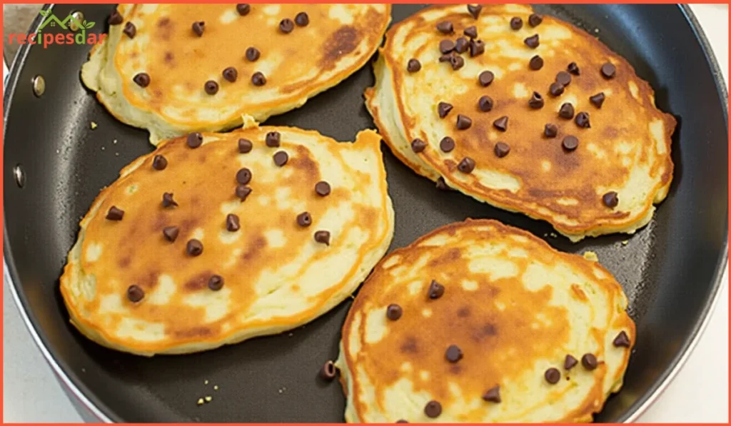 Golden sheet-pan chocolate chip pancakes sliced into squares, topped with fresh berries and a drizzle of maple syrup